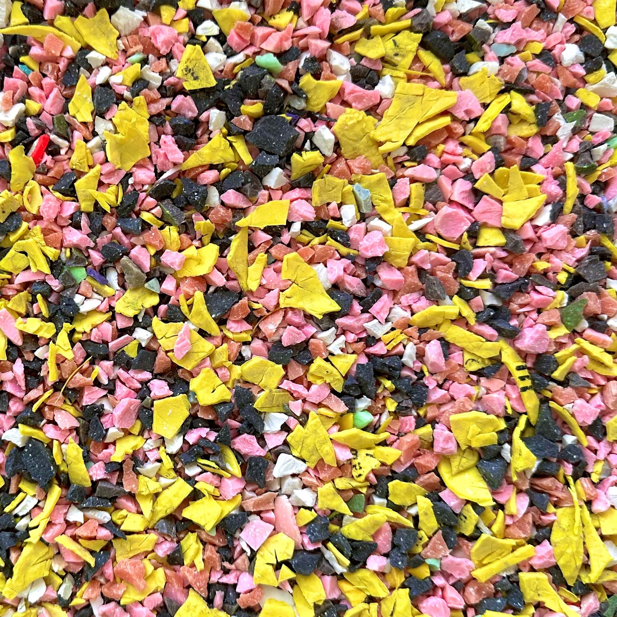 Shredded and recycled golf ball aggregate in colours of yellow, white, grey and pink.