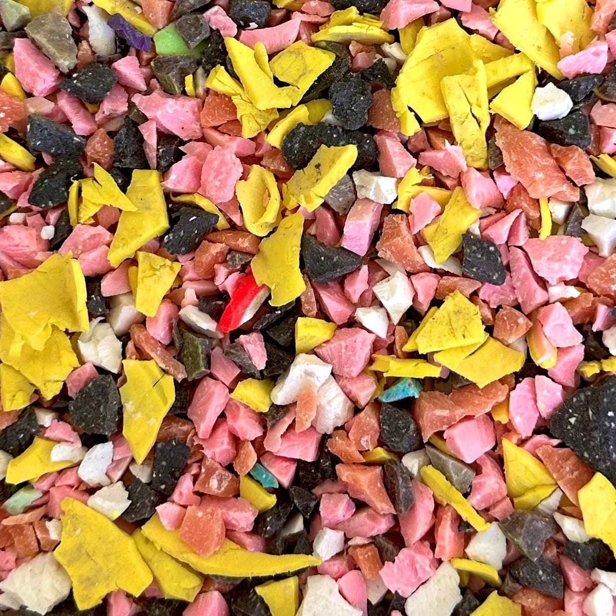 Shredded and recycled golf ball aggregate in colours of yellow, white, grey and pink.