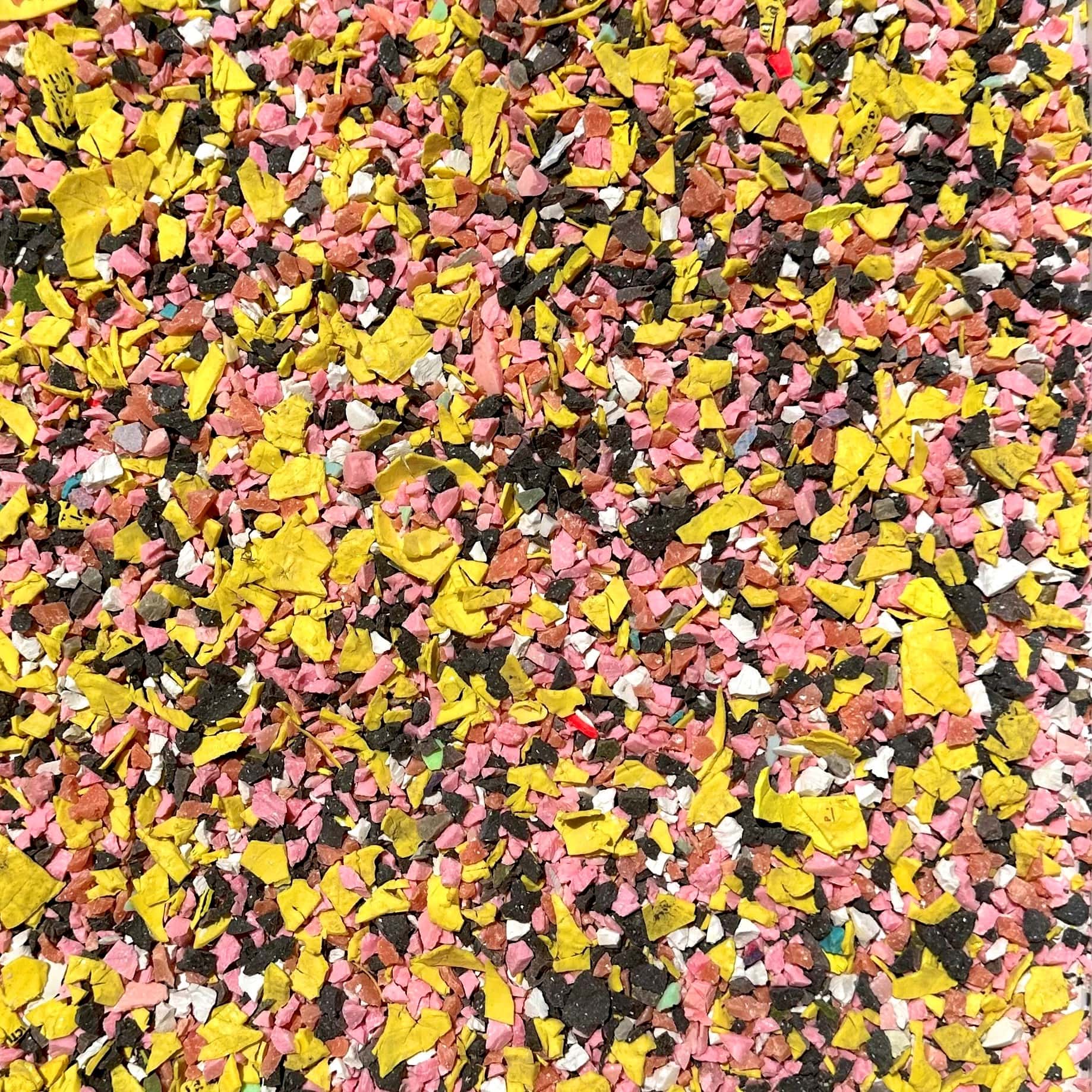 Shredded and recycled golf ball aggregate in colours of yellow, white, grey and pink.